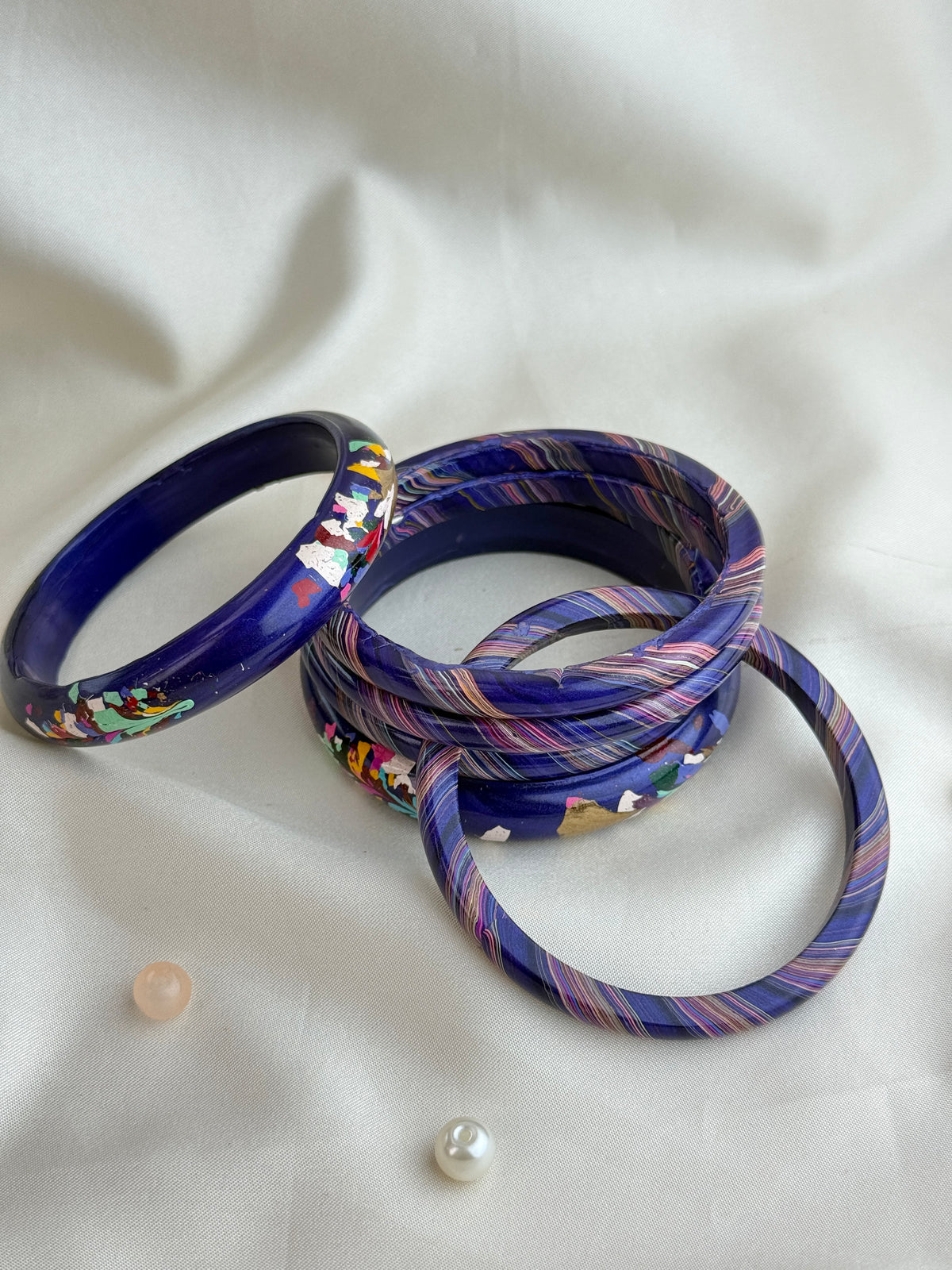 A set of five stacked acrylic bangles, featuring a deep blue base with colorful Japanese wave patterns and striped details in purple, pink, and white, displayed on a white fabric background.