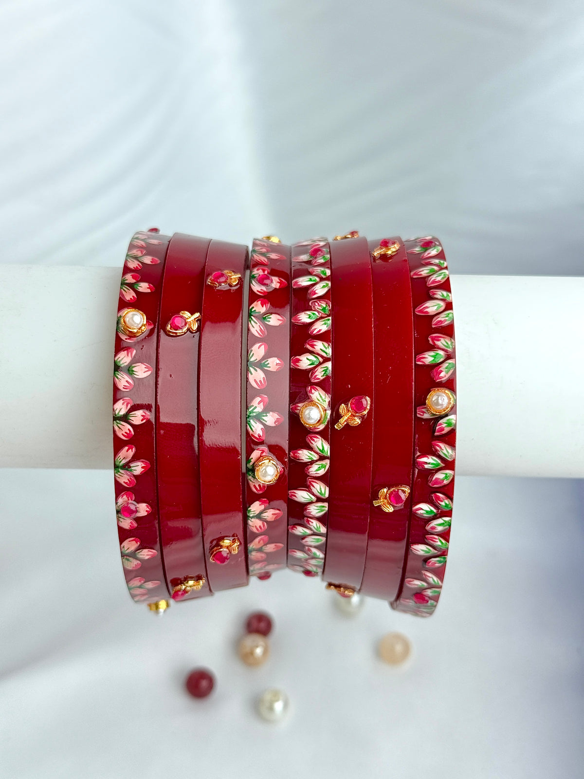A stack of red bangles with floral and paisley patterns, displayed on a white cylindrical stand against a white fabric background.