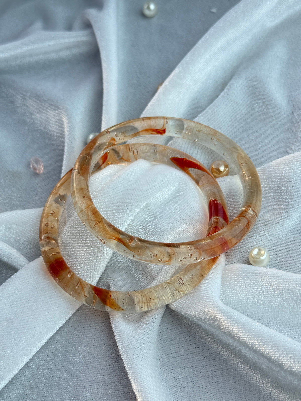 Two stacked translucent resin bangles with natural amber and reddish-brown inclusions, displayed on a white fabric backdrop.